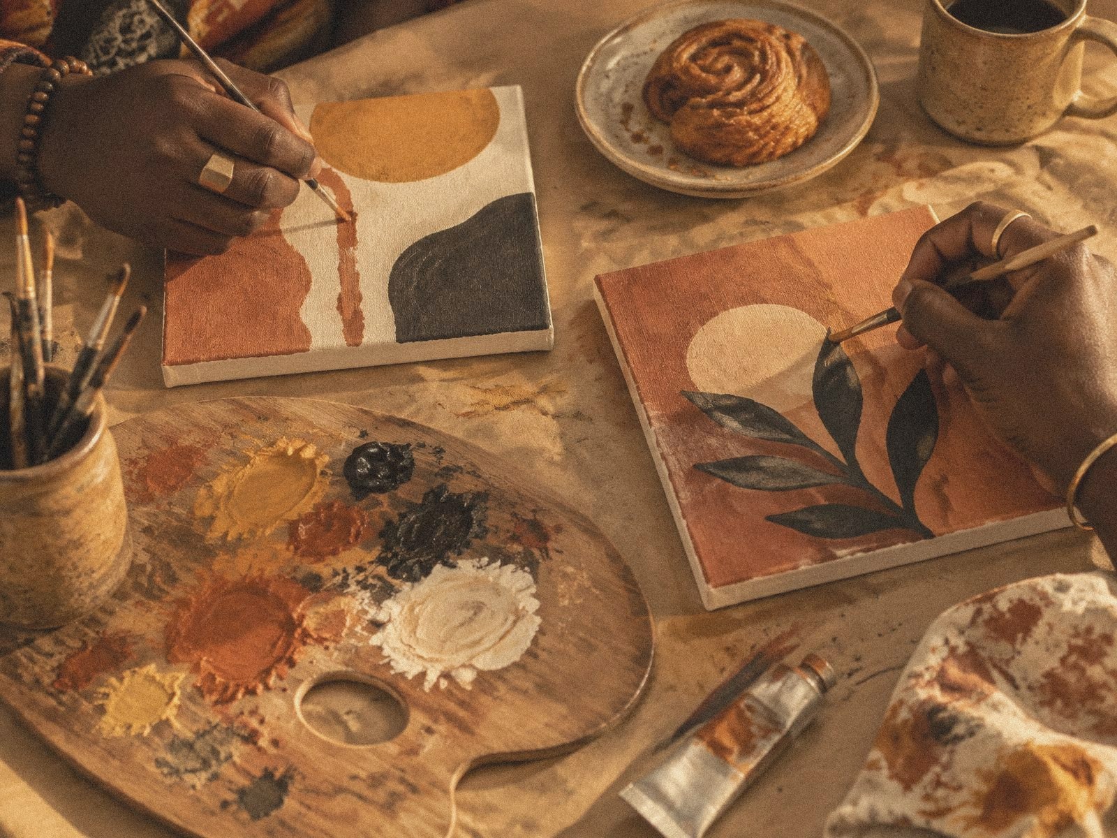 Hands arranging dried flowers beside a cup of tea on a wooden table in warm natural light